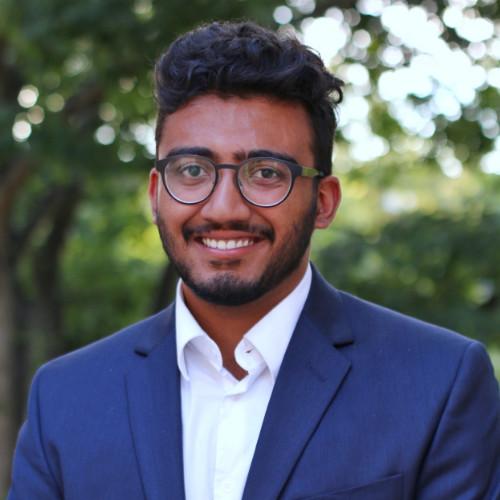 Adit in a navy suit and glasses, smiling — a professional headshot.